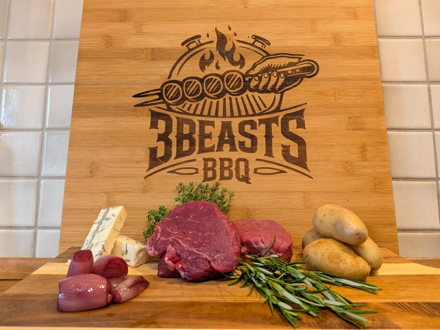 Bambusbrett mit 3Beasts-BBQ-Logo, Rinderfilet, Blauschimmelkäse und Rosmarin