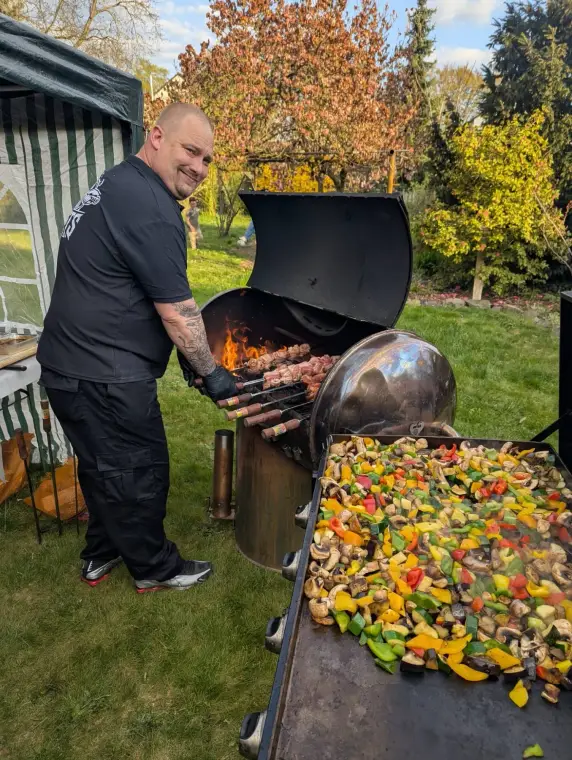 Koch am Fassgrill mit Spießen und Gemüse
